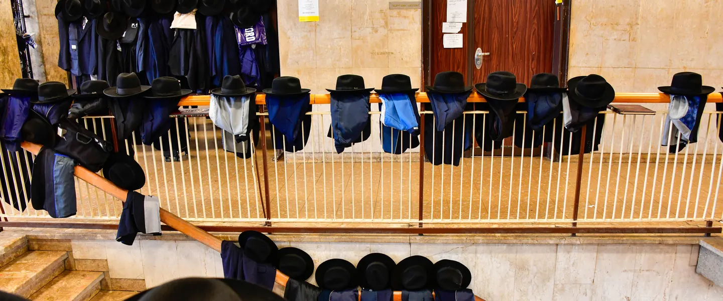 Hats and jackets resting along the stair rail outside the beis medrash