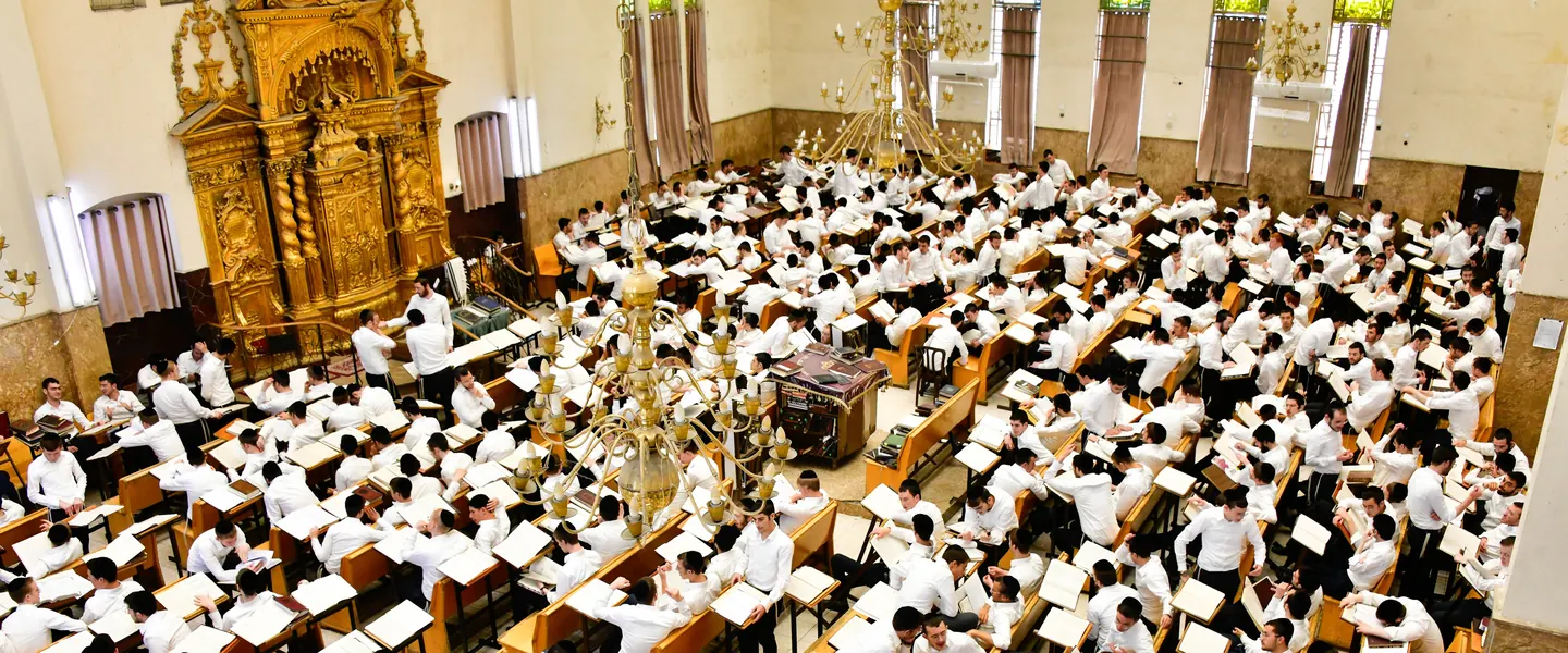 The main Ponevez beis medrash in full seder beneath its chandeliers
